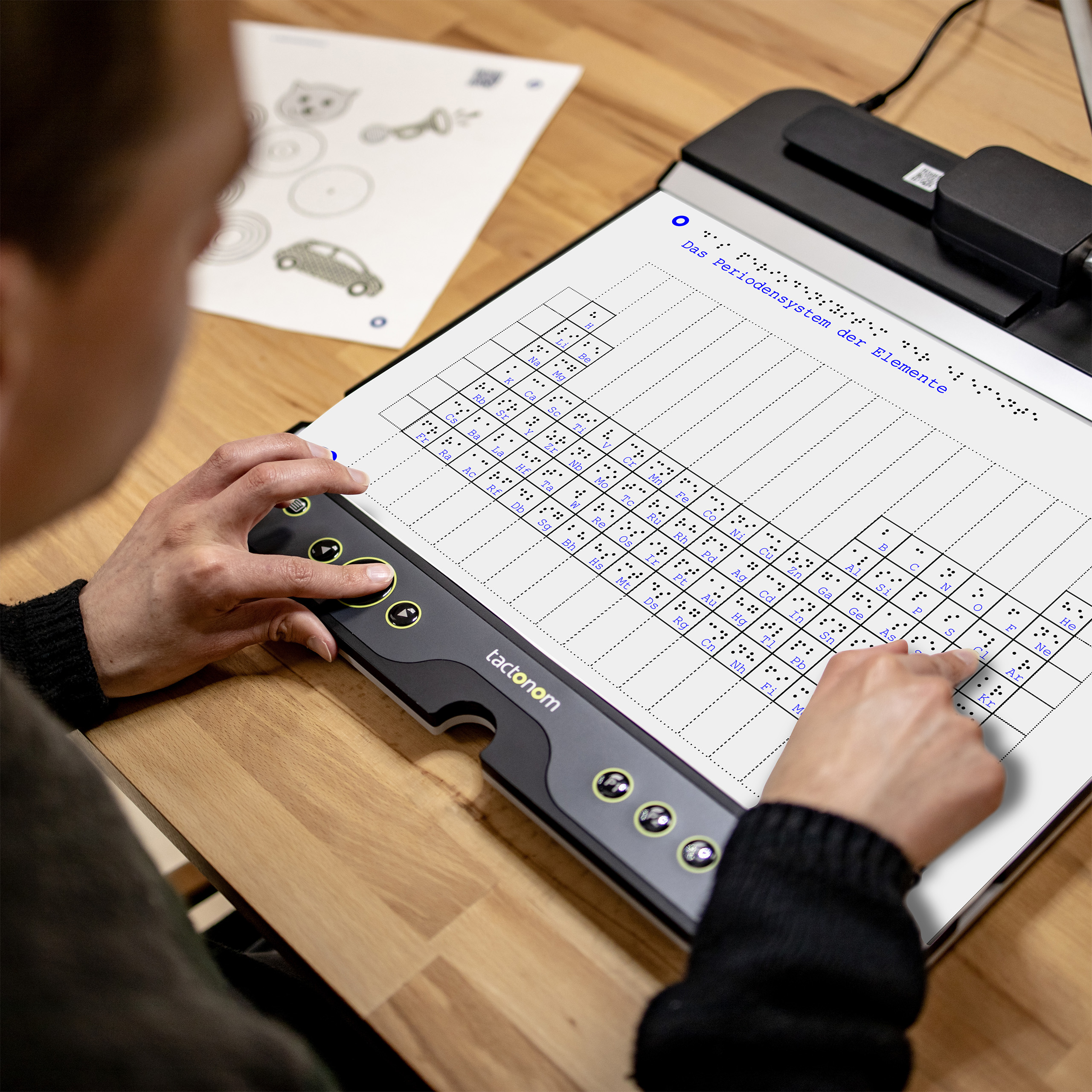 Un utilisateur s'assoit devant le lecteur Tactonom et sent le graphique "Le tableau périodique des éléments".